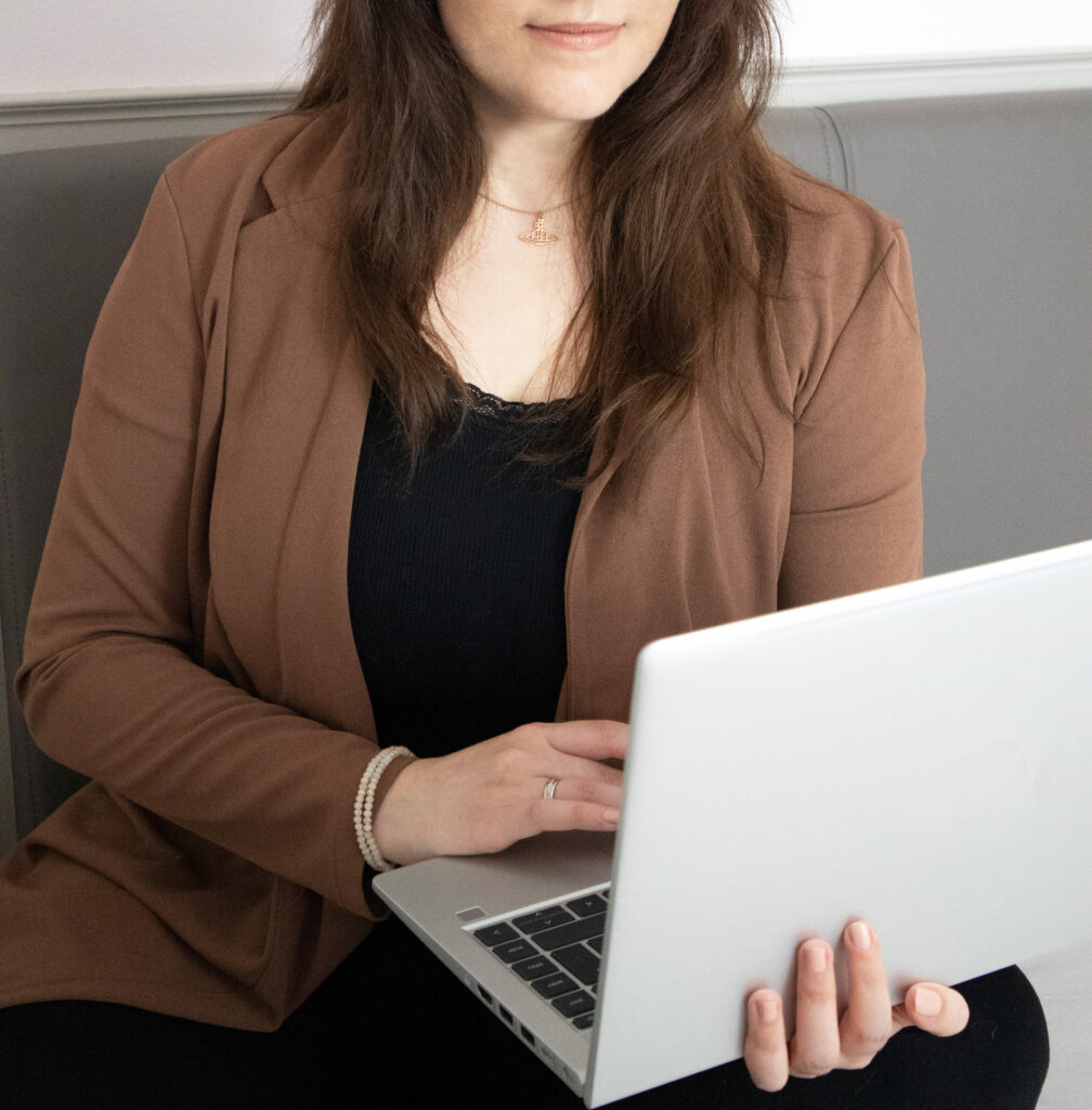 Der Bildausschnitt zeigt eine junge Frau - die freie Texterin - im Schneidersitz. Sie hält ihr Laptop in der Hand.