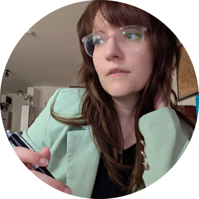 Die freie Texterin, Sarah Kreuzer, sitzt vor einem geöffneten Notizbuch und hat einen Stift in der Hand. Sie schaut nachdenklich zur Seite.