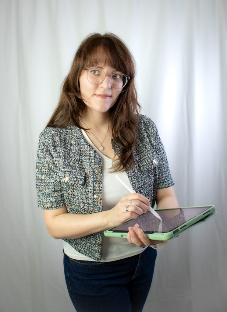 Die freie Texterin, Sarah Kreuzer, hat ihr iPad in der Hand und setzt mit dem iPen auf dem Display an. Sie schaut lächelnd zur Seite.