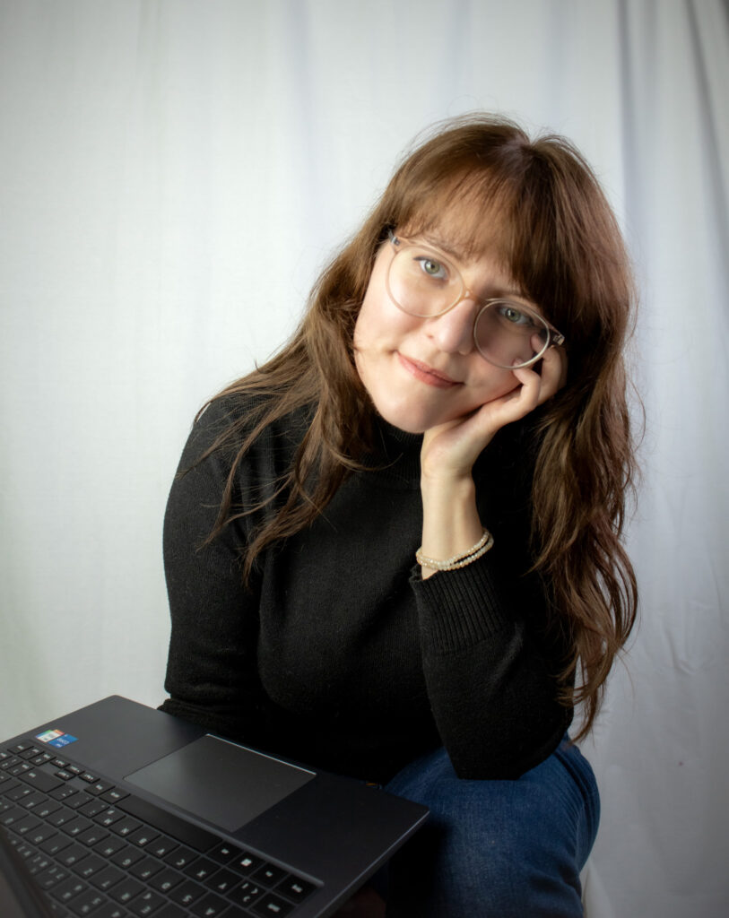 Die freie Texterin, Sarah Kreuzer, hat ihren Kopf an der Hand abgestützt und lächelt in die Kamera.