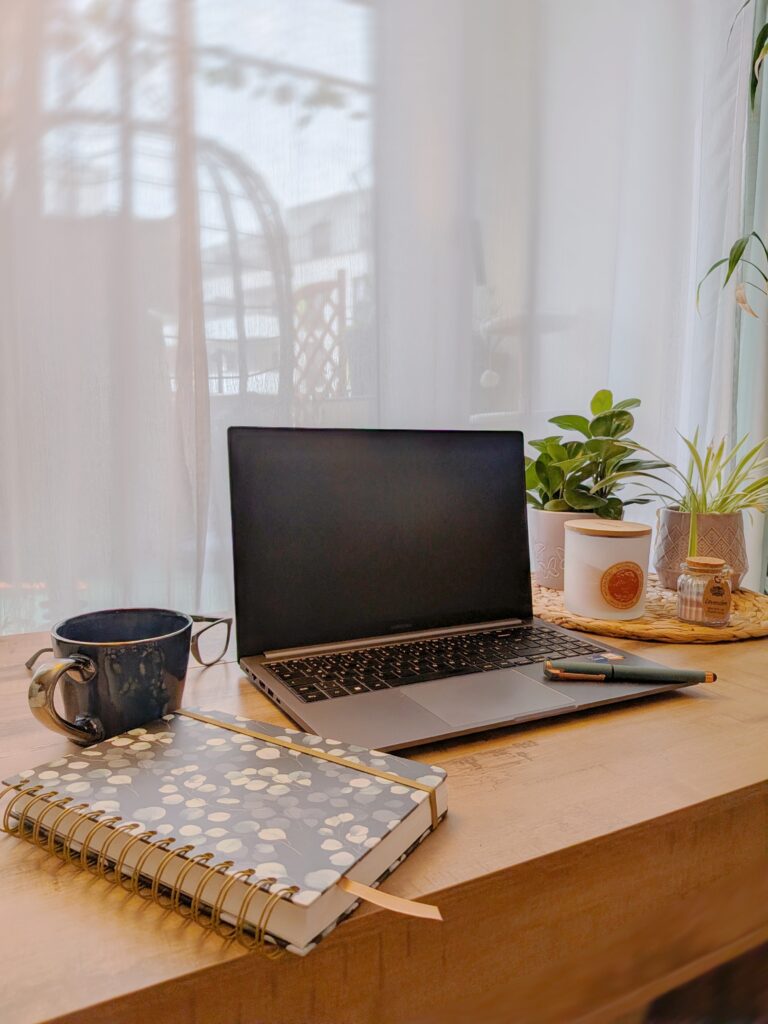 Sinnbild für Storytelling Marketing: Ein Laptop steht auf einem Schreibtisch. Links davon sind eine Kaffeetasse und ein Notizbuch. Auf der rechten Seite stehen einige Pflanzen und eine Kerze.