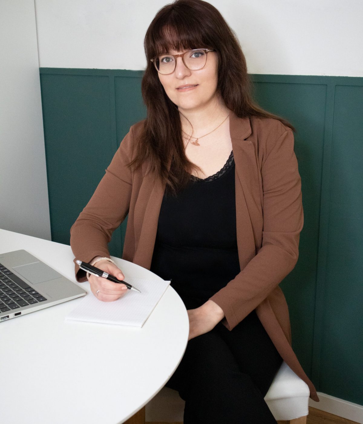 Die freie Texterin, Sarah Kreuzer, sitzt mit einem Laptop und einem Notizblock am Tisch und lächelt.
